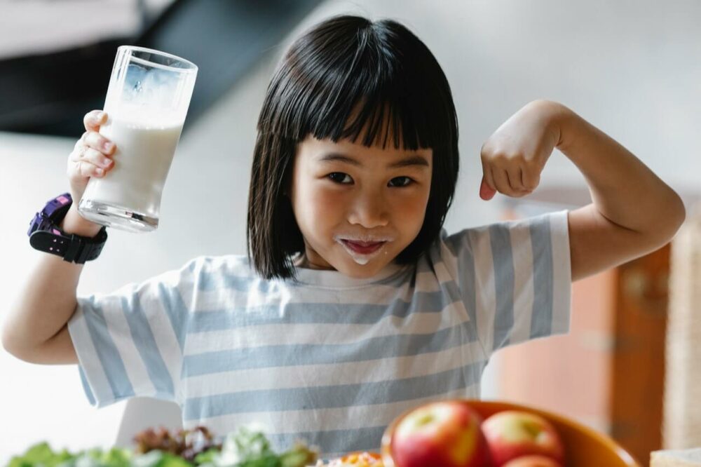 一個女孩一邊拿牛奶一邊比強壯手勢