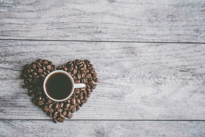 咖啡豆堆起一個心型形狀，上面有一杯黑咖啡