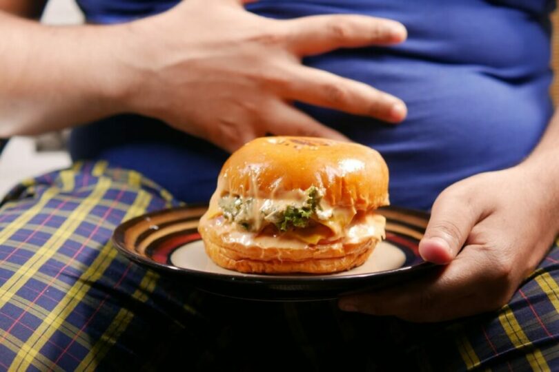 一個肥胖的人拿著一盤漢堡
