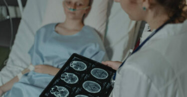 病人躺在病床上，看著醫生拿著腦部掃描圖
