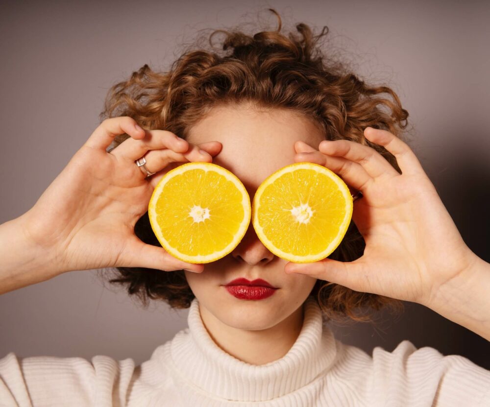 一個女生拿2片橘子在臉上